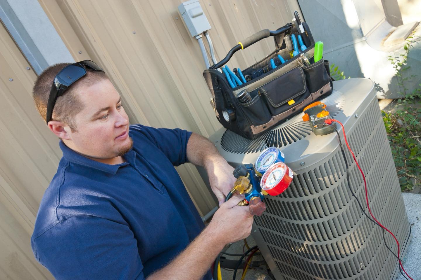HVAC technician checking AC refrigerant pressure with manifold gauges